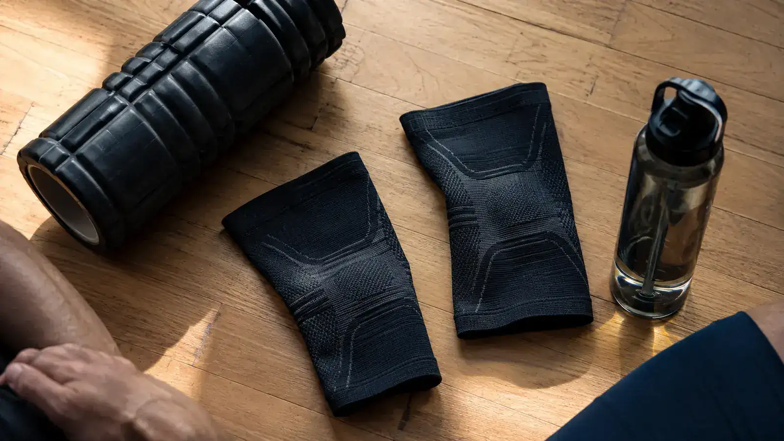 Pair of CAMBIVO knee sleeves laid flat next to a foam roller and water bottle, post-workout gear flatlay