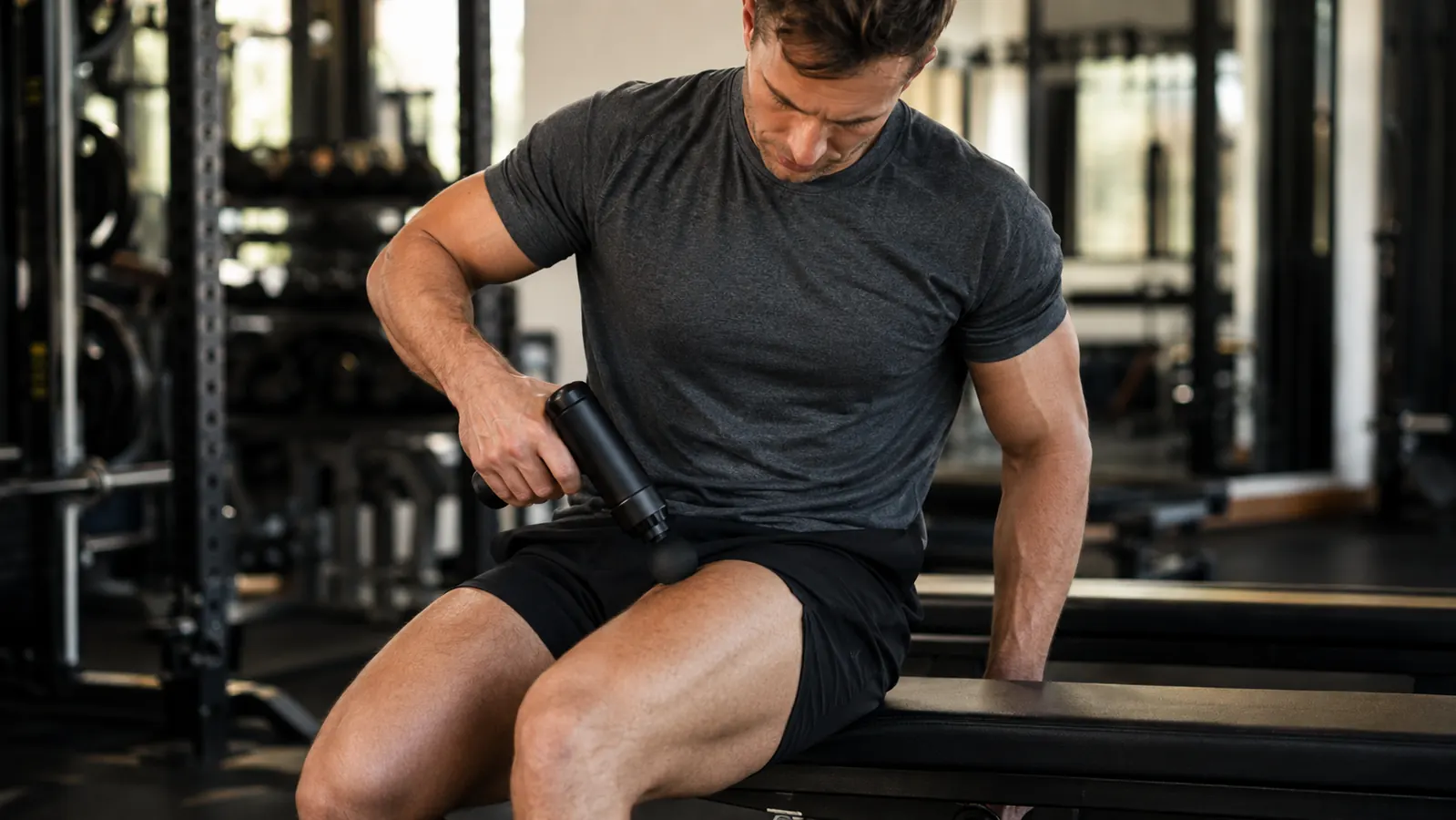 Man using a percussion massage gun on his quad muscle after a gym session