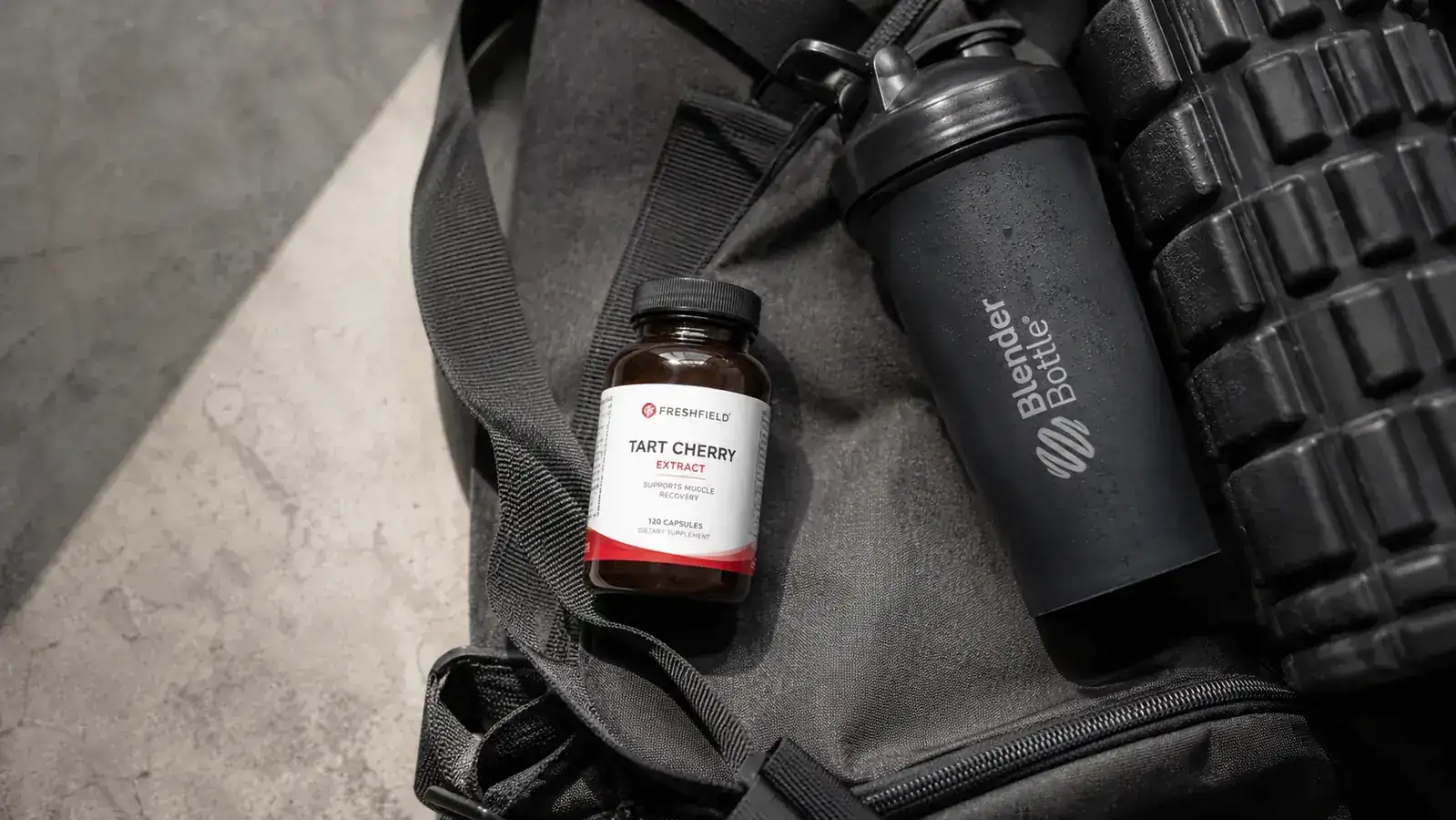 Tart cherry extract capsules on a gym bag next to a shaker bottle and a foam roller
