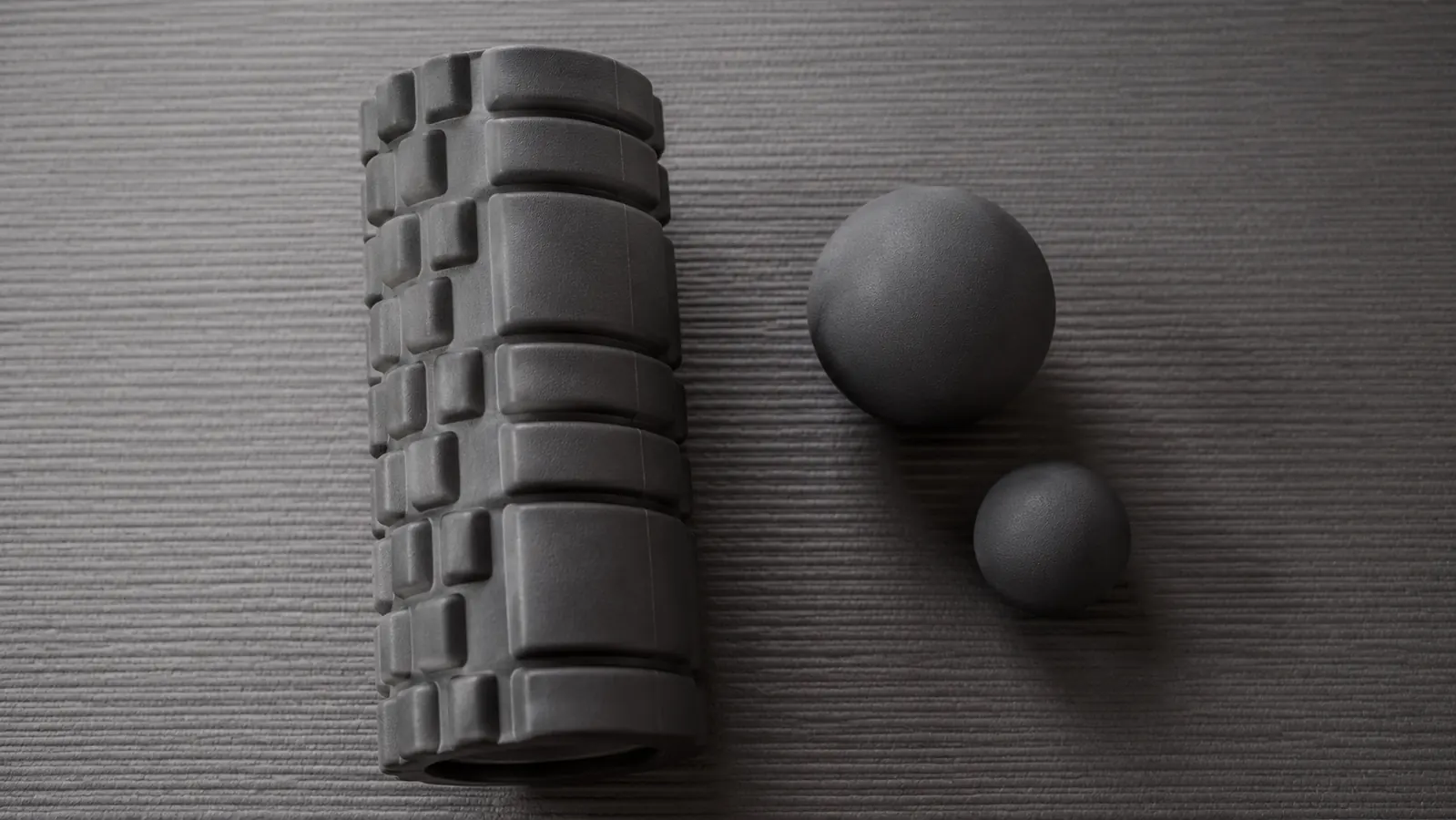 Side-by-side of a foam roller and two massage balls on a gym mat to illustrate size scale