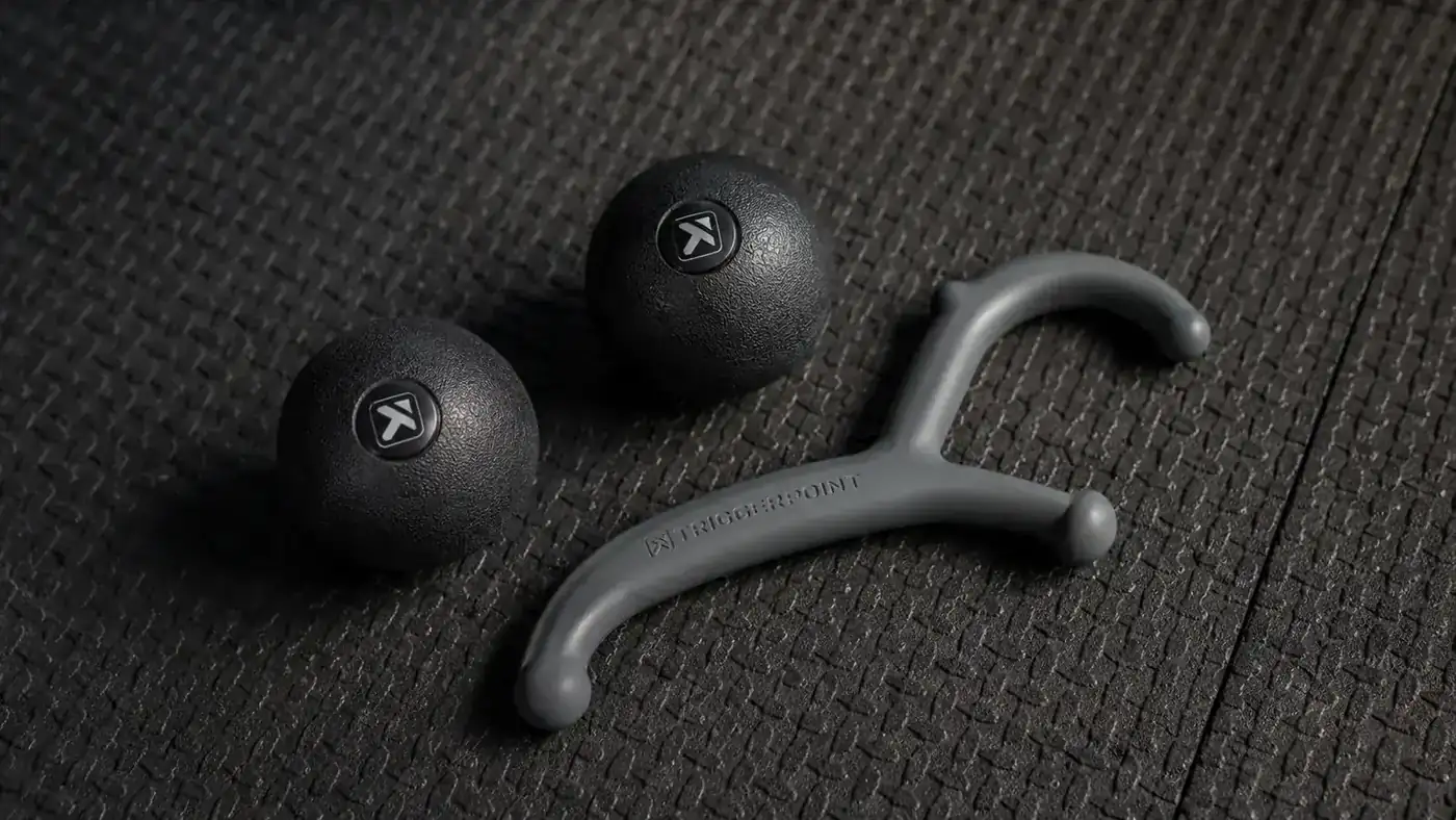 Two massage balls and a theracane-style hook tool laid out on a gym mat beside a water bottle