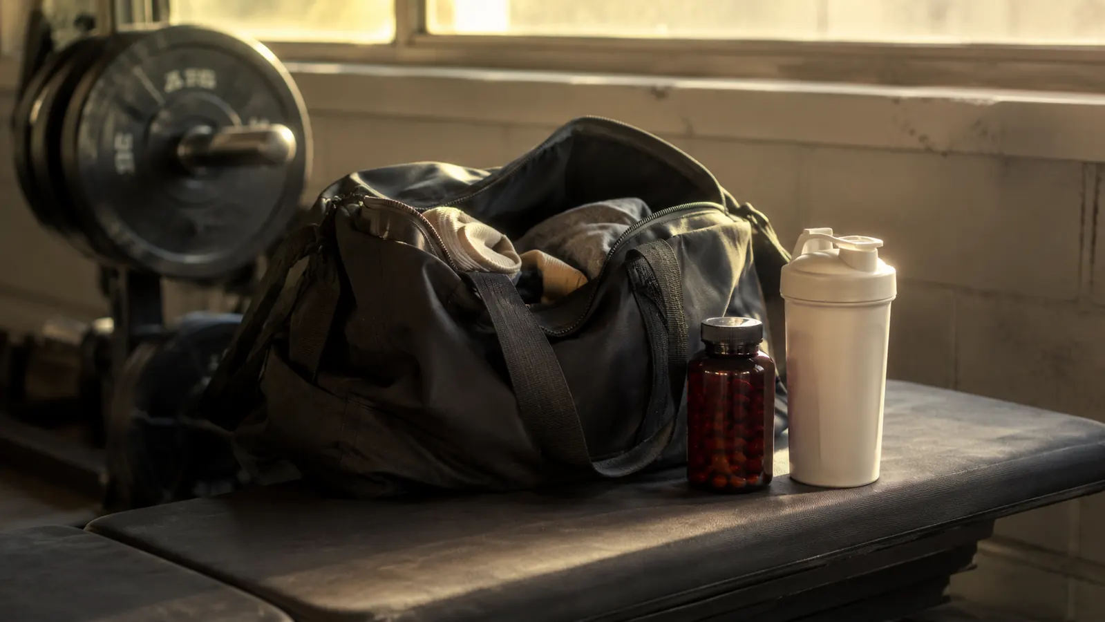 Tart cherry extract capsules next to a shaker bottle and gym bag on a weight room bench