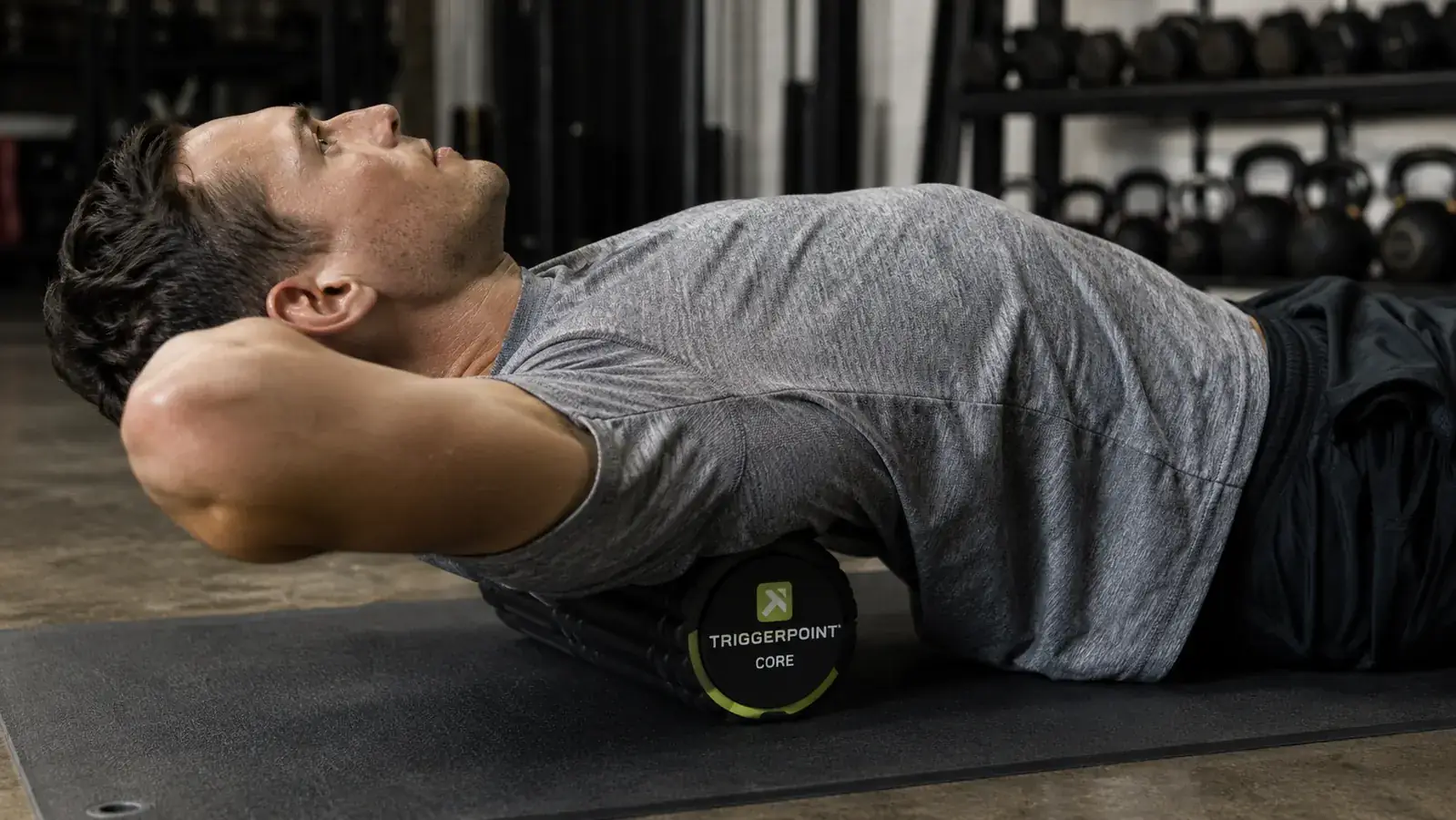 Person using a foam roller on their upper back, lying on a gym mat