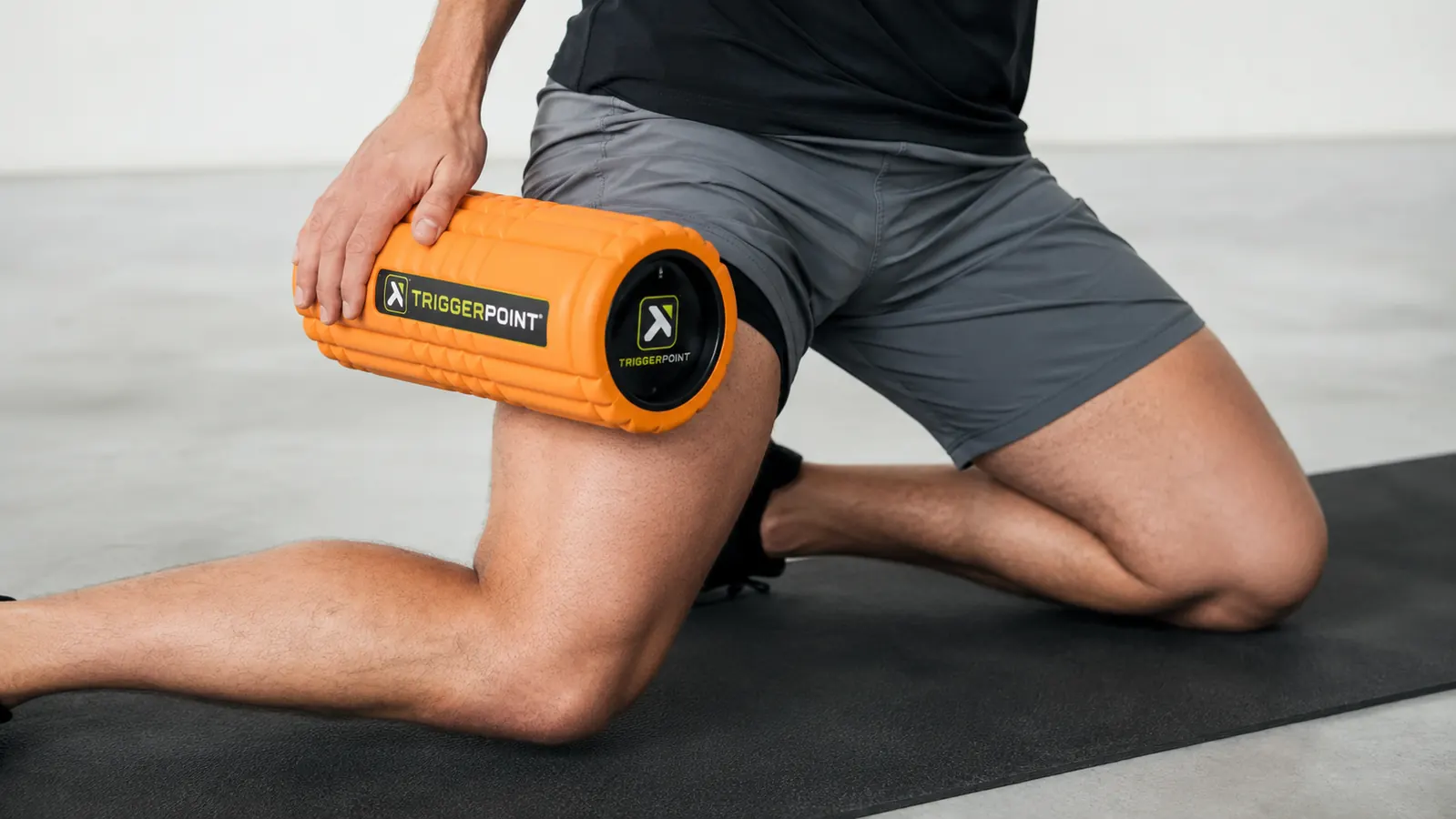 Close-up of hands pressing a TriggerPoint CORE foam roller against the front of the hip/quad area on a gym mat