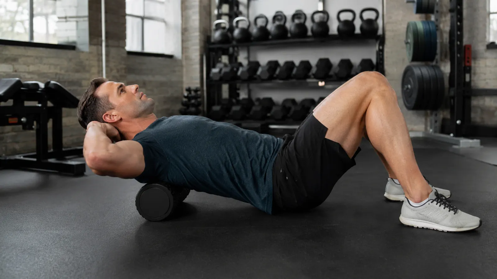 Person foam rolling their upper back on a gym floor after a workout