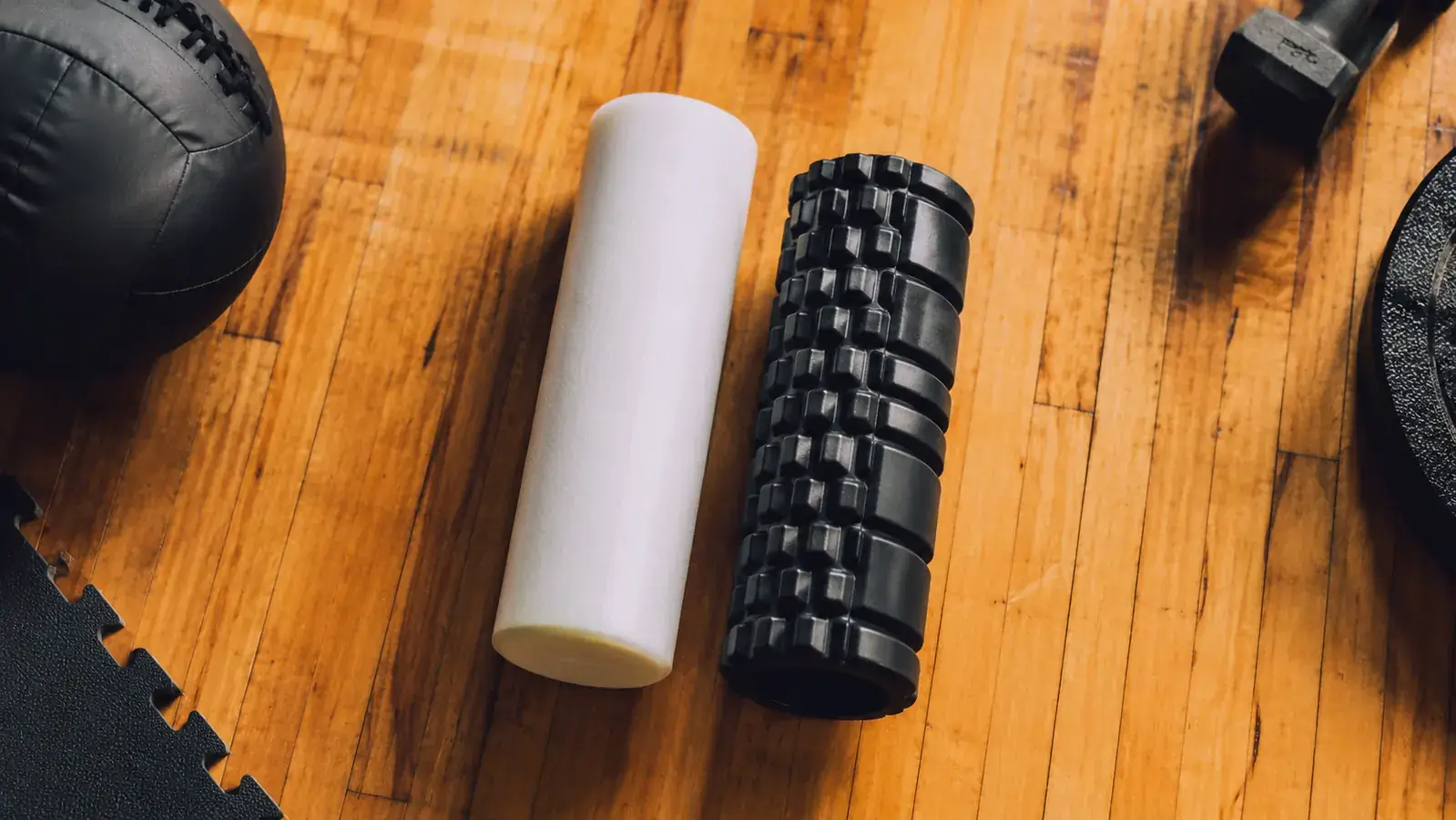 Two foam rollers side by side on a gym floor, one smooth and one with raised grid bumps